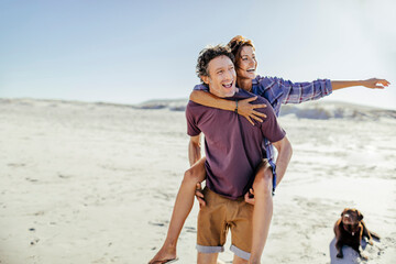 Couple enjoying playful piggyback ride on sunny beach