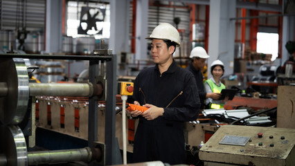 A man in a black suit and a white hat is standing in front of a machine. He is holding a red remote control