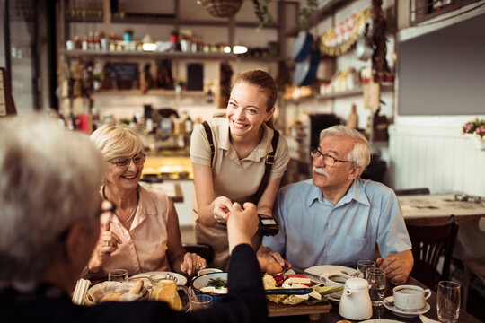 Senior woman paying with smartphone for meal with friends at restaurant
