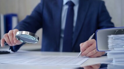 Businessman is carefully examining financial documents with a magnifying glass, highlighting the...