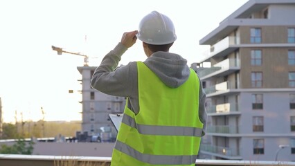 Male constructive engineer with a white protective helmet and safety vest is writing on a clipboard...
