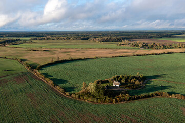 Fototapeta premium Aerial view of a secluded cottage surrounded by vibrant green fields in early morning light