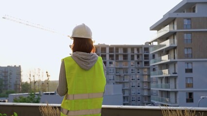 Construction female engineer taking notes and writing on clipboard while inspecting a building site at sunset