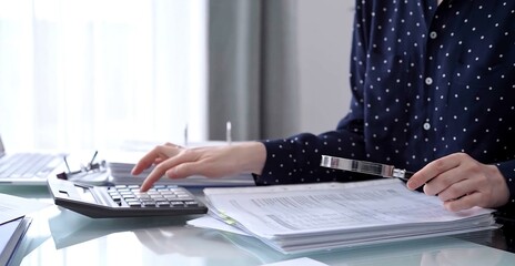 Businesswoman using calculator and reviewing ring folder of financial documents with magnifying glass at desk in modern office. Audit and taxes in business