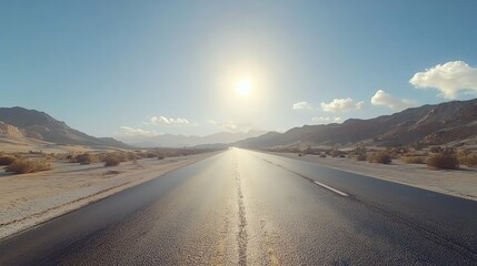 A tranquil highway stretches into the horizon under a clear blue sky, with mountains and sunlight illuminating the vast desert landscape.