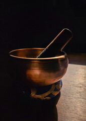 A close-up shot of a Tibetan singing bowl in soft natural light, casting deep shadows, highlighting its bronze tones and texture. A calming representation of meditation and peace
