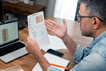 Man reviewing utility bill at home with laptop and notepad on table. Concept of household finance...