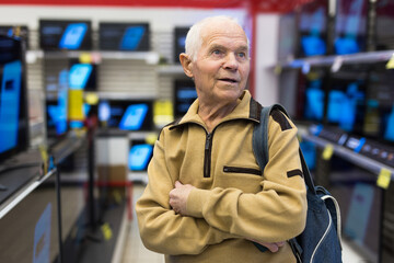 Obraz premium Elderly man choosing TV in showroom of electronics store