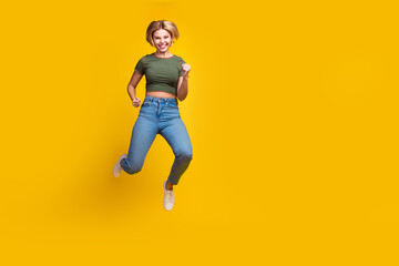 Full size photo of good mood optimistic girl dressed khaki crop top jeans running clenching fists isolated on yellow color background