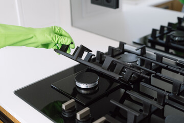 A person in green gloves hold metal grid over clean and black gas stove on kitchen