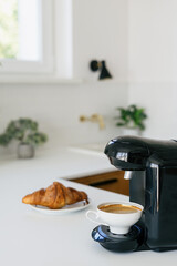 Cup of espresso and freshly baked croissant on kitchen counter