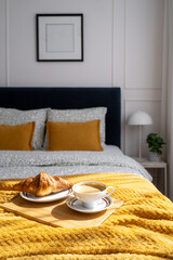 Breakfast in a cozy bedroom featuring a croissant and coffee on a wooden tray with yellow bedding