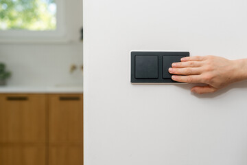 Hand pressing a modern black light switch in a minimalistic kitchen