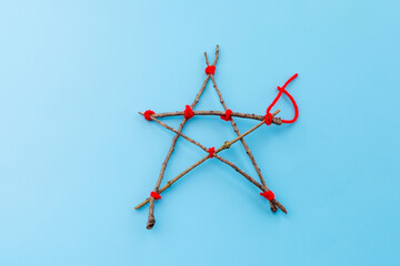 Step-by-step tutorial on making a star-shaped ornament from sticks and red yarn. Craft DIY collage with materials and hands tying knots. Christmas decoration concept, blue background, top view