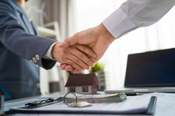 Two men shake hands in front of a desk with a contract on it
