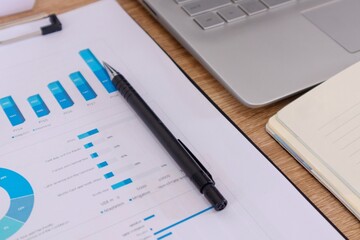 Close up view of workplace with notebook, pen, laptop, and paperwork or report