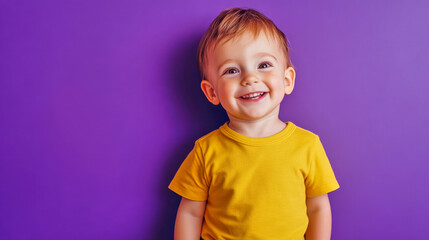 Naklejka premium Happy smiling toddler boy in a yellow shirt on a purple background enjoying his time indoors