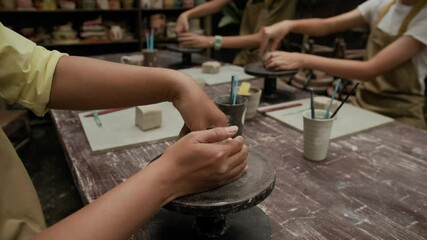 Cropped shot of anonymous pottery class visitors modeling clay at table in workshop