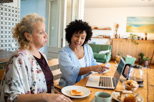 Middle aged lesbian couple discussing finances with laptop at breakfast table
