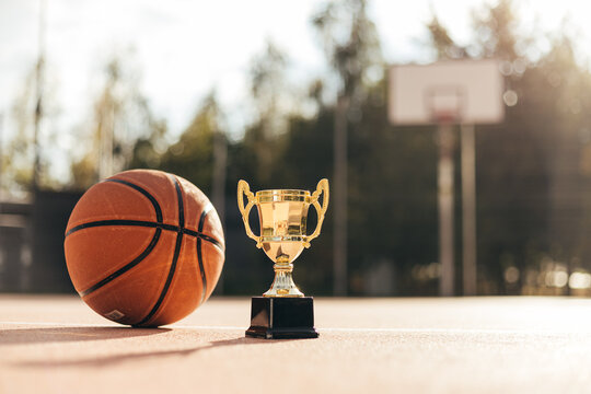 Basketball ball and golden cup on rubber playground close up, street basketball competition
