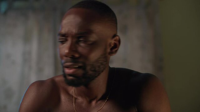 Shirtless African man wakes up from a nightmare at night as a result of stress and anxiety.