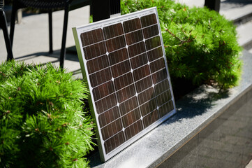 Photovoltaic solar panel against backdrop of vibrant green shrubs on stone ledge, soaking up...