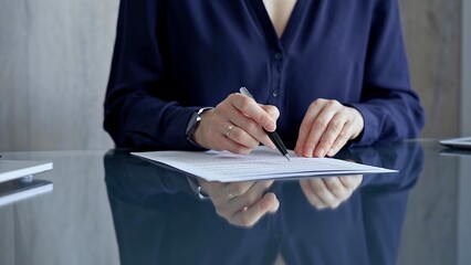 Businesswoman in dark blue blouse signing contract at the table. Close-up of a male executive signing a legal document on a glass desk. Business people concept