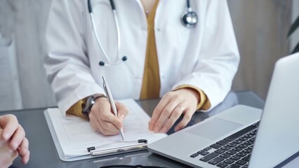 Doctor completing paperwork with patient. Close-up of a doctor's hands with forms, imparting information to a laptop. Medicine and health care concept
