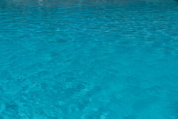 Sky blue water in a swimming pool with light reflections. Sunlight refraction on clear turquoise surface of a swimming pool. Relaxing transparent flowing water. Caustic turquoise pattern.