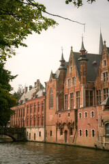 Bright red brick buildings with small towers next to a canal in a summer day in Bruges, Belgium
