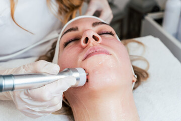 Young woman receiving modern radio-frequency face tightening treatment. Most popular non-invasive...