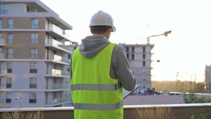 Man engineer with a white protective helmet and safety vest is writing on a clipboard while...
