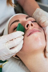 Beautiful woman with smooth healthy skin is getting face massage using jade facial stone. Modern and popular skincare treatment concept.