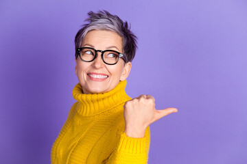 Photo of adorable funny woman yellow knitwear looking pointing thumb back empty space isolated violet color background