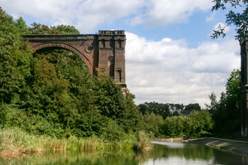 Old viaduct bridge covered with green trees and bushes next to a pond.