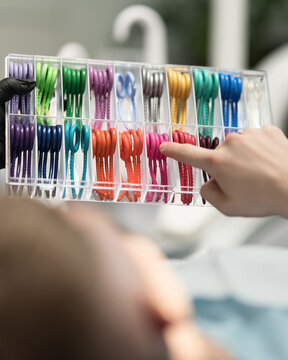 Colorful orthodontic ligatures in hands of patient in dental office. Set of brightly colored rubber bands for braces. Front view. Copy Space.