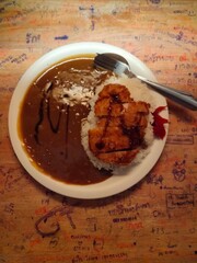 A delicious plate featuring crispy fried chicken atop fluffy rice, served with a rich curry sauce. The colorful background adds a playful touch, making this meal visually appealing and appetizing.