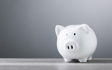 A white piggy bank sits on a wooden table against a grey background, with ample copy space for text. The image symbolizes savings, financial planning, and responsible money management.
