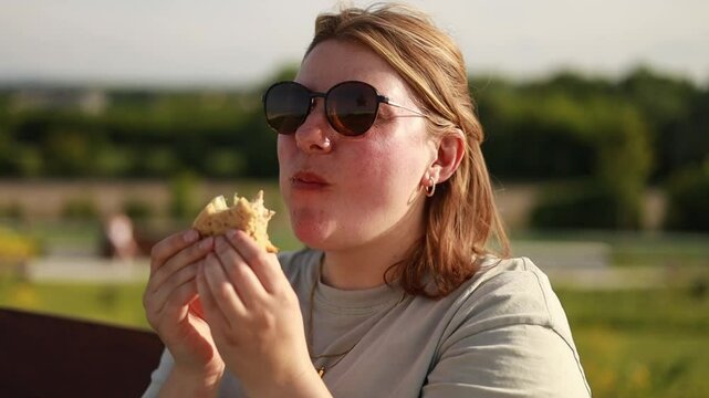 White woman eating sandwich on sunset, golden hour, epic summer scene, picnic, sun glasses on face, enjoyed woman's face, summer vibes, sunset in park, peaceful outdoor meal, overweight, chubby woman