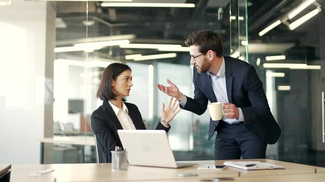 Businessman in formal suit sexually harasses a young female coworker at workplace in business office. Adult male employee flirts with a shocked worried woman colleague who has an expression of concern