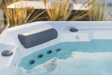 Modern bath with hydromassage jet, comfortable headrest and clear blue water in tub