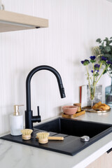 Modern kitchen sink with black faucet, dish soap and wooden brush