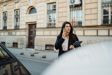 Fototapeta premium Young businesswoman talking on smartphone on the street on way to work