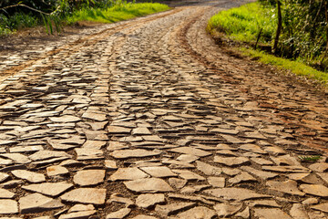 Road in a rural area made of irregular stones, with an orange hue at sunrise.