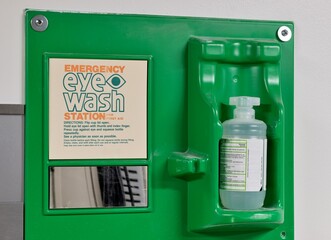 Emergency eye wash station safety kit on wall with bottle and mirror.
