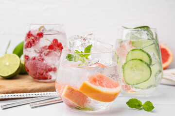 Different refreshing drinks in glasses on white tiled table, closeup