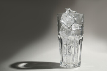 One glass with ice for refreshing drink on grey background
