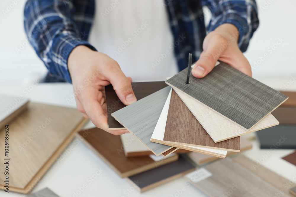 Poster Man choosing wooden flooring among different samples at table, closeup