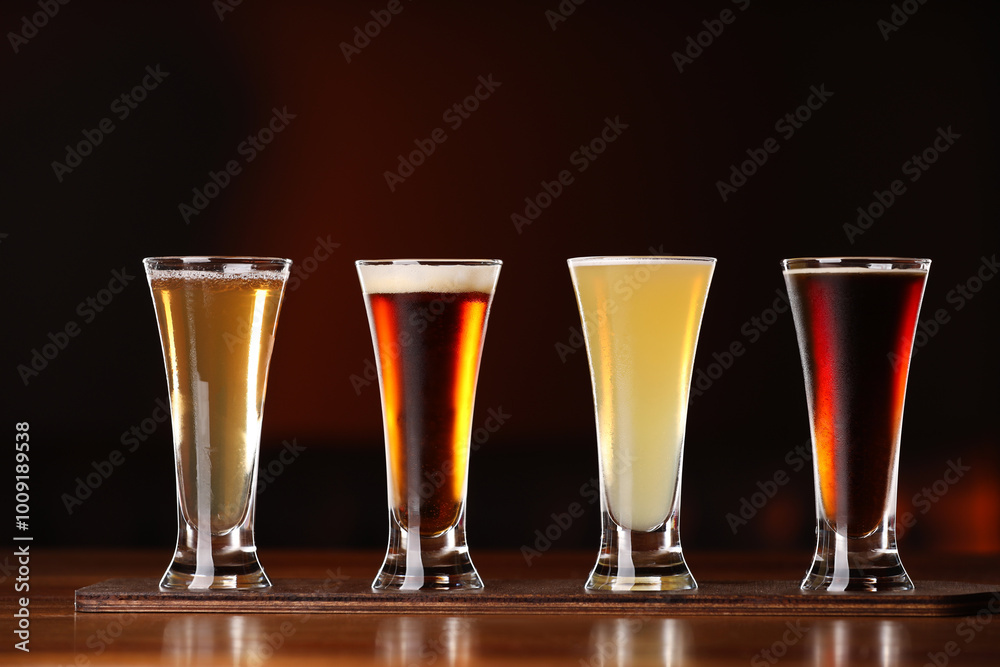 Sticker Glasses with different types of beer on wooden table against color background