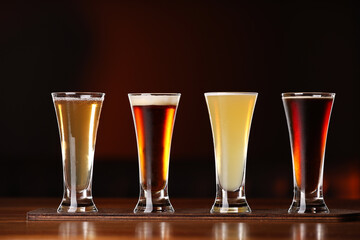 Glasses with different types of beer on wooden table against color background